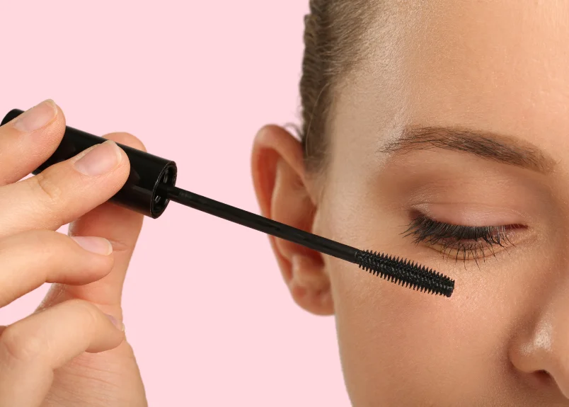 Woman applying mascara and pink background