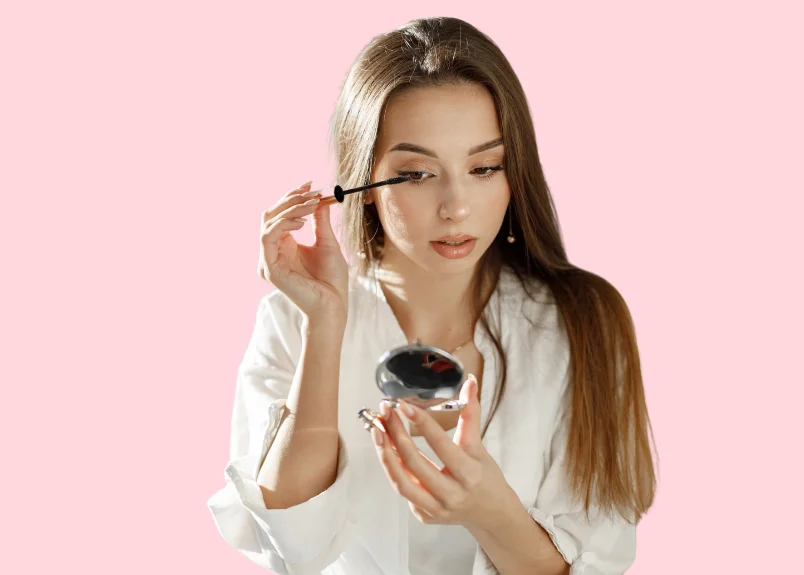 A beautiful woman with mascara wand and mirror in hand