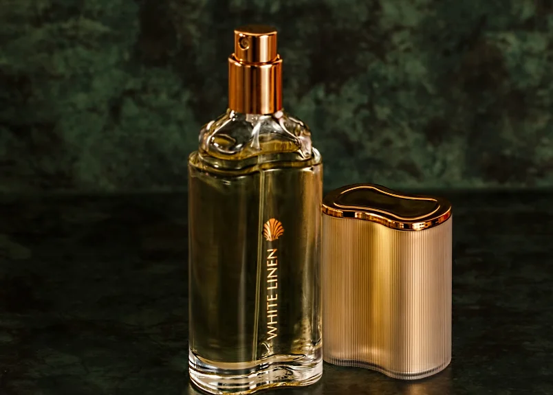 An unlided bottle of perfume with its lid on a granite surface